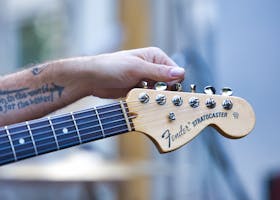 Detailed image of a hand holding a Fender Stratocaster guitar neck with tattoo visible.